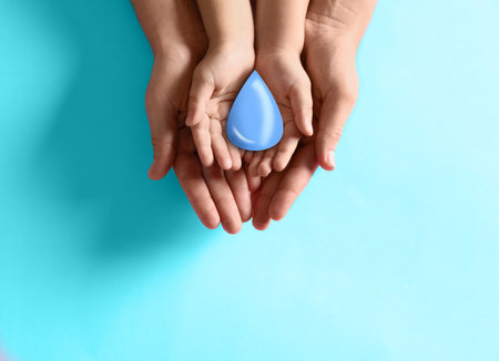 Mother and her child holding water drop on light blue background, top view. Ecology protectionの写真素材