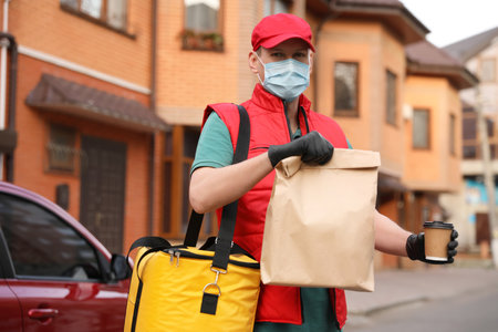 Courier in protective mask and gloves with orders near car outdoors. Food delivery service during...