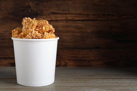 Bucket with yummy nuggets on table against wooden background, space for textの写真素材