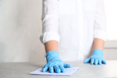 Woman in gloves wiping gray marble table with rag indoors, closeup