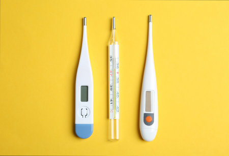 Different thermometers on yellow background, flat lay
