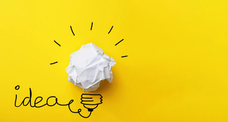 idea concept. Composition with crumpled paper ball and drawing of lamp bulb on yellow background,...