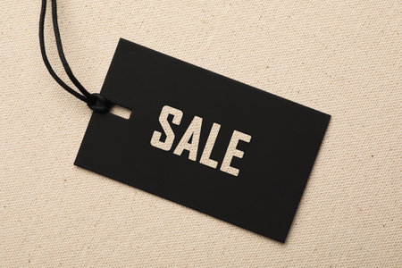 Tag with text SALE on color fabric background, top view. Black Friday