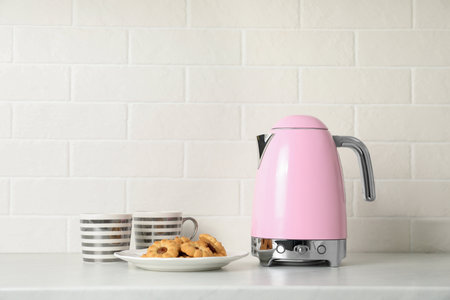 Modern electric kettle, cups and cookies on counter in kitchenの写真素材