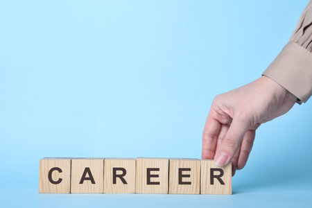 Woman making word CAREER with wooden cubes on light blue background, closeup. Space for textの写真素材