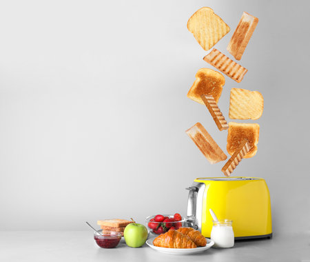 Slices of grilled wheat bread flying out of toaster on light grey tableの写真素材