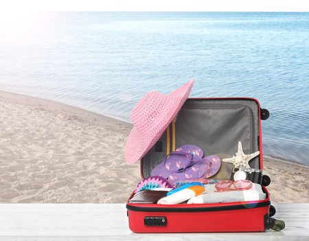 Suitcase with different beach objects on wooden table near sea. Space for textの写真素材