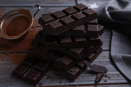 Tasty dark chocolate bars and sieve with cocoa powder on wooden tableの写真素材