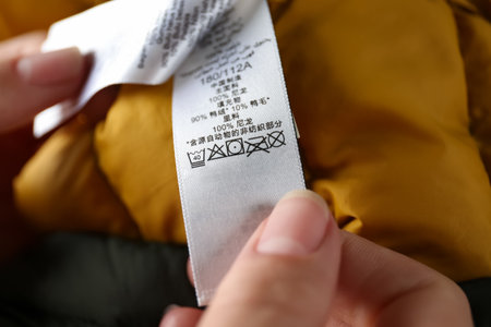 Woman reading clothing label with care symbols and material content on color jacket, closeupの写真素材