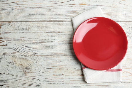 Empty red plate and napkin on white wooden table, flat lay. Space for textの写真素材
