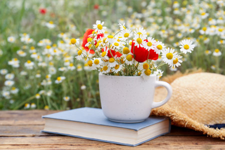 Composition with chamomiles, poppies, straw hat and book on wooden table outdoorsの写真素材