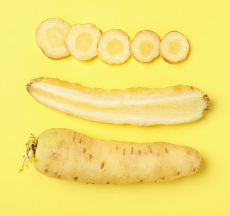 Whole and cut raw white carrots on yellow background, flat layの写真素材