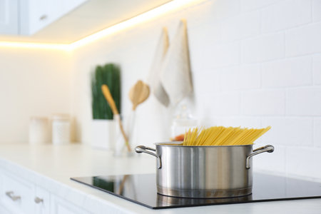 Saucepan with uncooked pasta on stove in kitchenの写真素材