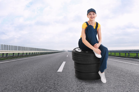 Mechanic in uniform with car tires on asphalt highway outdoors, space for textの写真素材