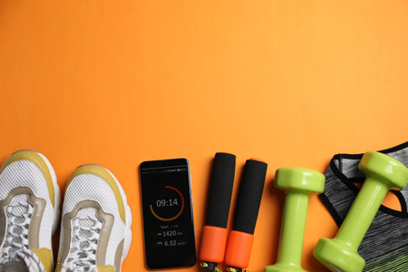Flat lay composition with fitness equipment and smartphone on orange background, space for textの写真素材