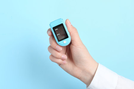 Woman holding modern fingertip pulse oximeter on light blue background, closeupの写真素材