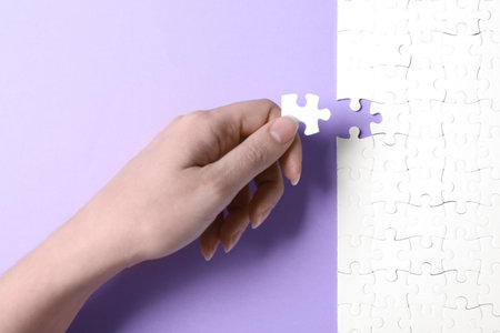 Woman putting last piece of white puzzle on violet background, closeupの写真素材