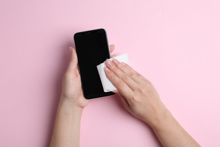 Woman cleaning mobile phone with antiseptic wipe on pink background, top viewの写真素材