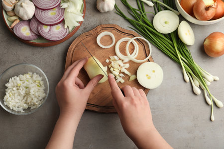 Woman cutting fresh onion on wooden board at gray table, top viewの写真素材