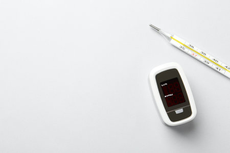 Modern fingertip pulse oximeter and mercury thermometer on white background, flat lay. Space for textの写真素材