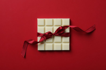Tasty white chocolate bar with ribbon on red background, top viewの写真素材