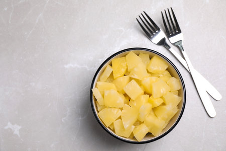 Tasty canned pineapple pieces and forks on light gray marble table, flat lay. Space for textの写真素材