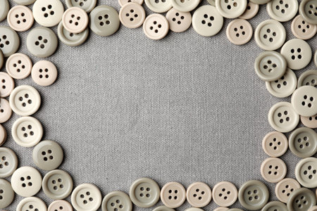 Frame of plastic sewing buttons on gray fabric, flat lay. Space for text