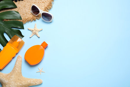 Flat lay composition with sun protection products and beach accessories on light blue background....
