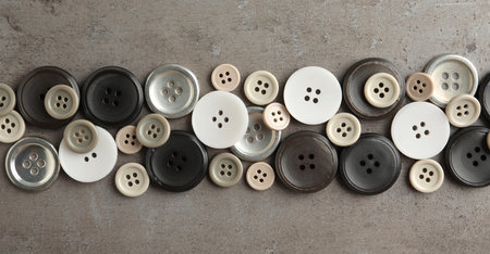 Many plastic sewing buttons on gray background, flat lay