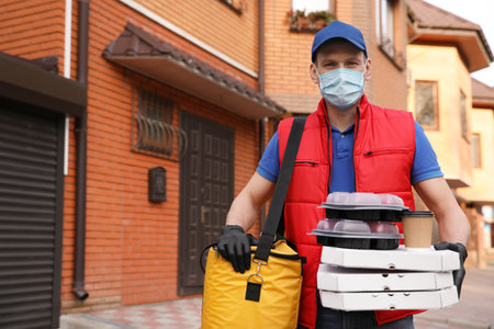 Courier in protective mask and gloves with orders near house outdoors.の写真素材