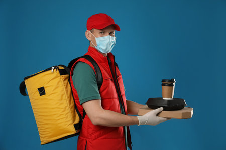 Courier in protective mask and gloves holding order on blue background.の写真素材