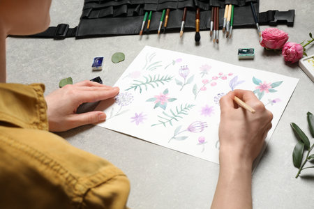 Woman painting flowers with watercolor at gray stone table, closeup