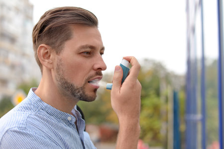Man using asthma inhaler outdoors. health care