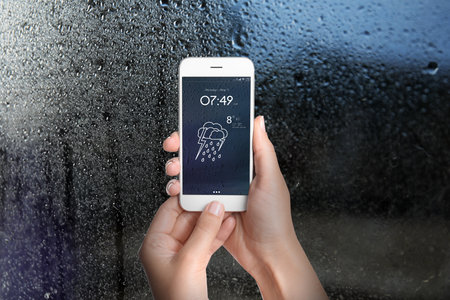 Woman using weather forecast app on smartphone near window indoors, closeupの写真素材