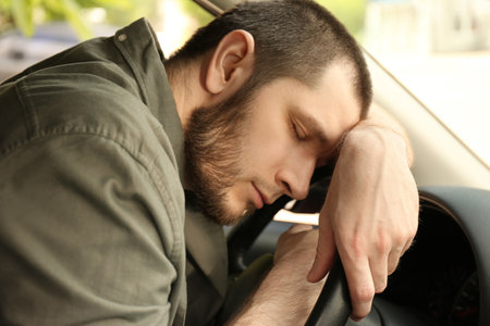 Tired man sleeping on steering wheel in his carの写真素材