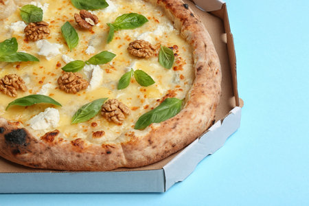Delicious cheese pizza with walnuts and basil in takeout box on light blue background, closeupの写真素材