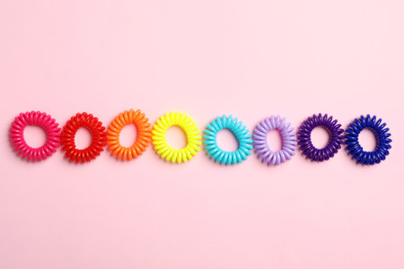 Colorful spiral rubber bands on pink background, flat lay