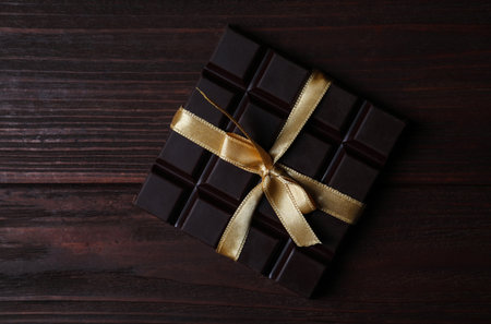 Tasty dark chocolate bar with ribbon on wooden table, top viewの写真素材