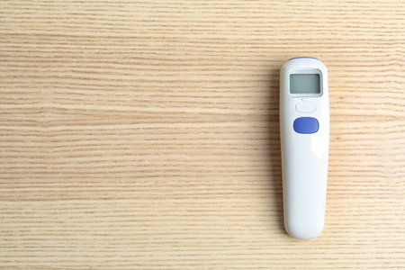 Modern non contact thermometer on wooden table, top view. Space for text