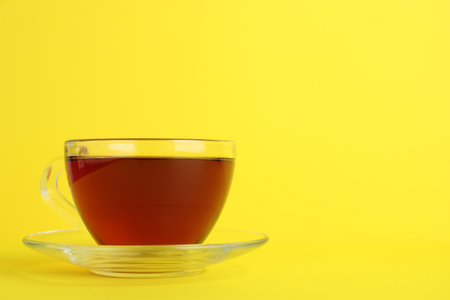Glass cup of aromatic black tea on yellow background, space for textの写真素材