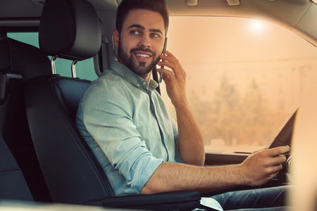 Handsome young man talking on smartphone while driving his car