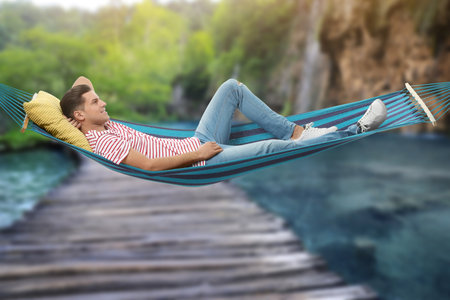 Man resting in hammock near waterfall on sunny dayの写真素材