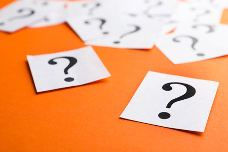 Paper notes with question marks on orange background, closeupの写真素材