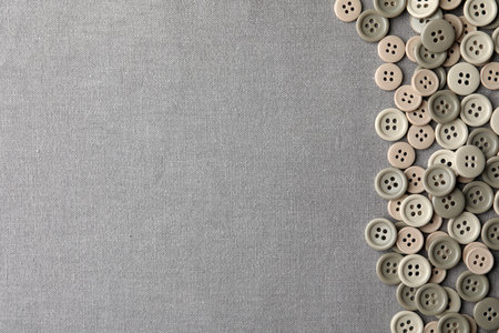 Many plastic sewing buttons on gray fabric, flat lay. Space for text