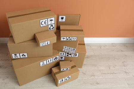 Cardboard boxes with different packaging symbols on floor near orange wall. Parcel deliveryの写真素材