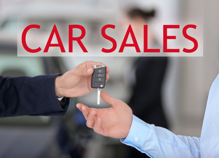 Young salesman giving car key to client against blurred background, closeupの写真素材