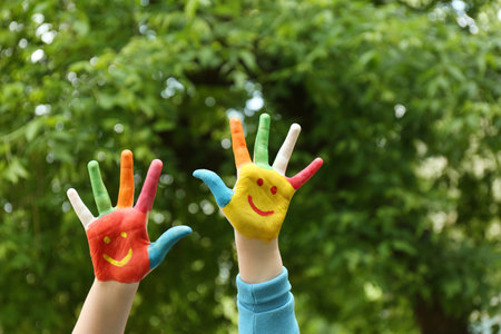 Kid with smiling faces drawn on palms in green park, closeupの写真素材