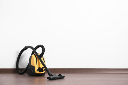 Modern yellow vacuum cleaner on wooden floor near white wall, space for textの写真素材