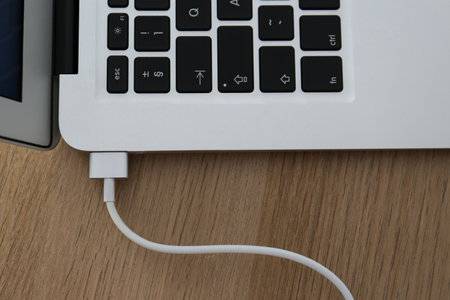 Modern laptop charging on wooden table, closeup
