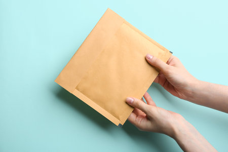 Woman holding kraft paper envelope on light blue background, closeupの写真素材